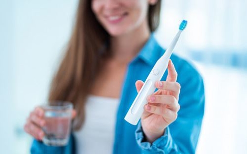 Woman holding electric toothbrush and glass of water.